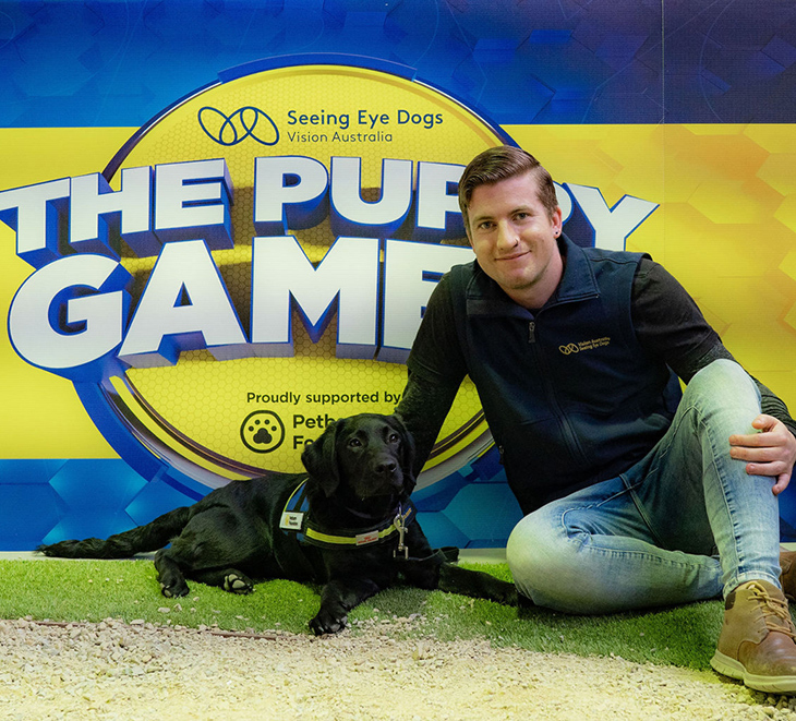 Chessy and trainer Jack sitting in front of Puppy Games sign