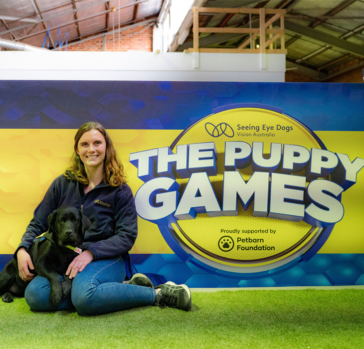 Paige and Frieda sitting on grass next to Puppy Games sign